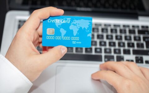 Person holding credit card near laptop for online shopping, emphasizing secure online transactions.