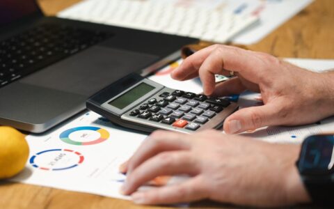 A person analyzing financial data using a calculator and laptop on a desk.
