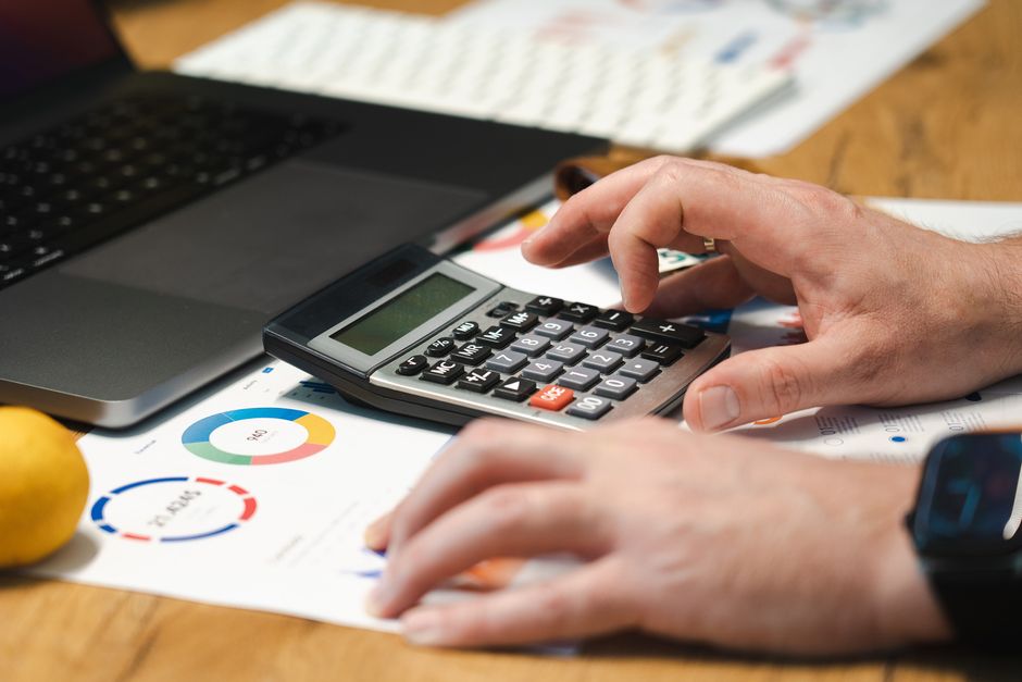A person analyzing financial data using a calculator and laptop on a desk.