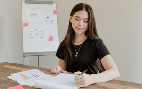 Young woman analyzing data and preparing a report at a wooden desk.