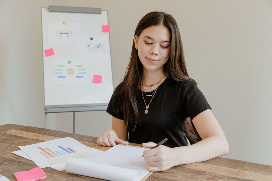 Young woman analyzing data and preparing a report at a wooden desk.