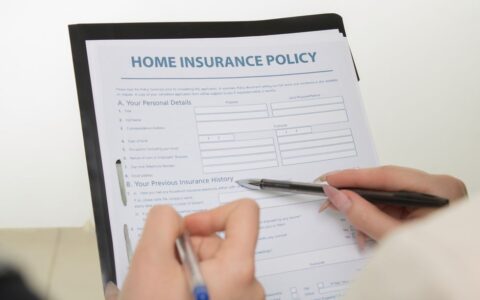 Hands holding pens filling out a home insurance policy document for coverage details.