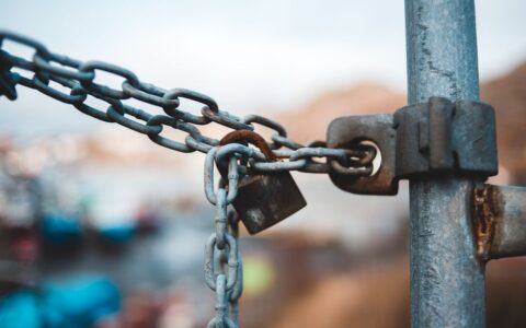 Old metal chain with rustic lock hanging on fence on street against blurred background in daytime