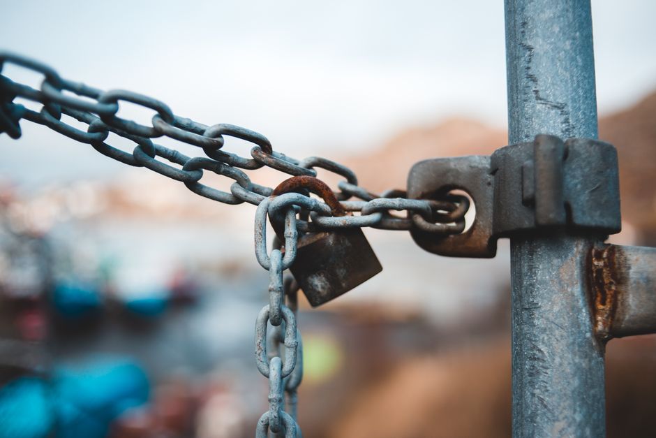 Old metal chain with rustic lock hanging on fence on street against blurred background in daytime