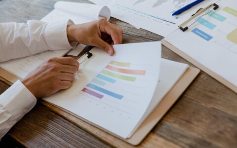 Close-up of hands reviewing business report with colorful charts and graphs on a wooden desk.