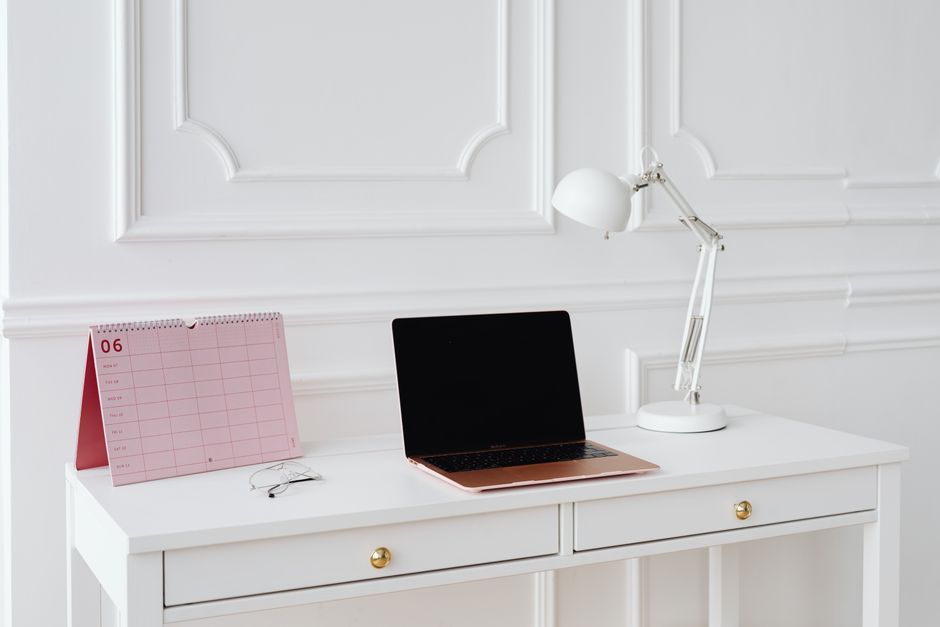 Simple desk setup with laptop, calendar, and lamp in a bright, minimalist office setting.