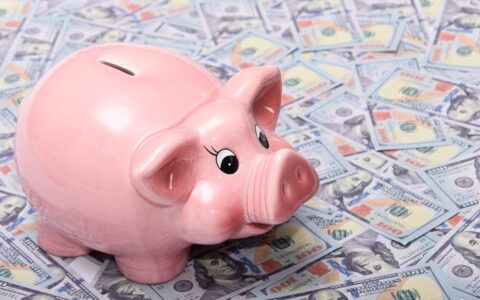 Pink ceramic piggy bank placed on a spread of US dollar bills symbolizing savings and financial security.