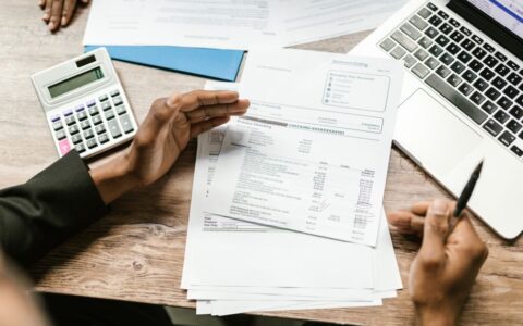 Hands holding financial documents with calculator and laptop on office desk, business analysis scene.