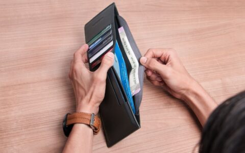 Close-up of a person managing a wallet with cash and cards on a wooden table.