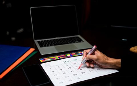 A person plans on a calendar at a desk with a laptop and phone, May 2022.