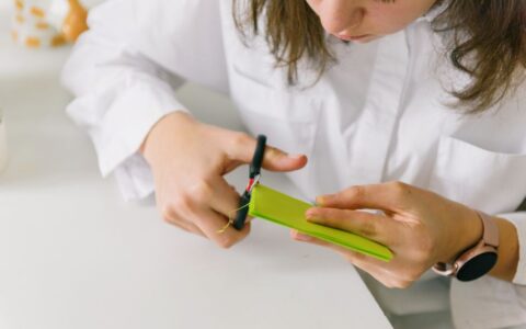A teenager engaged in a crafting project using scissors and colored paper indoors.