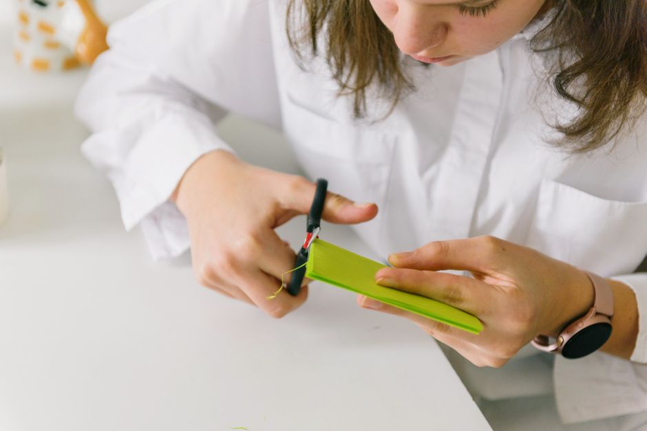 A teenager engaged in a crafting project using scissors and colored paper indoors.