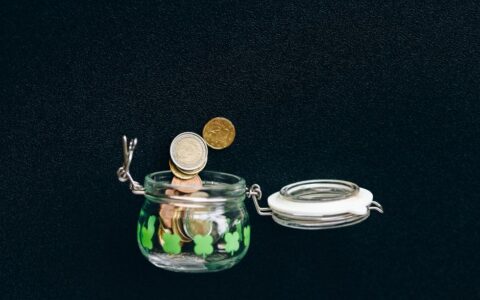 Glass jar with coins falling into it on a black background, symbolizing savings.